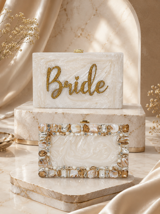 A white marble-style bridal keepsake box set with a gold glitter 'Bride' script on the front, displayed on a marble pedestal with a matching rectangular box and a rhinestone-trimmed frame piece in a warm beige studio setting.
