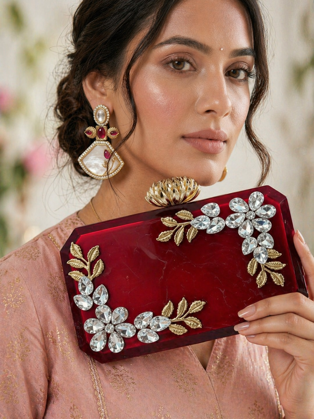 Woman holding a red clutch with floral and leaf designs, wearing traditional jewelry.