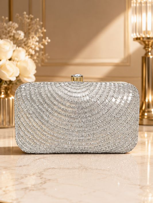 Silver beaded clutch on a reflective surface with decorative flowers and lamp in the background